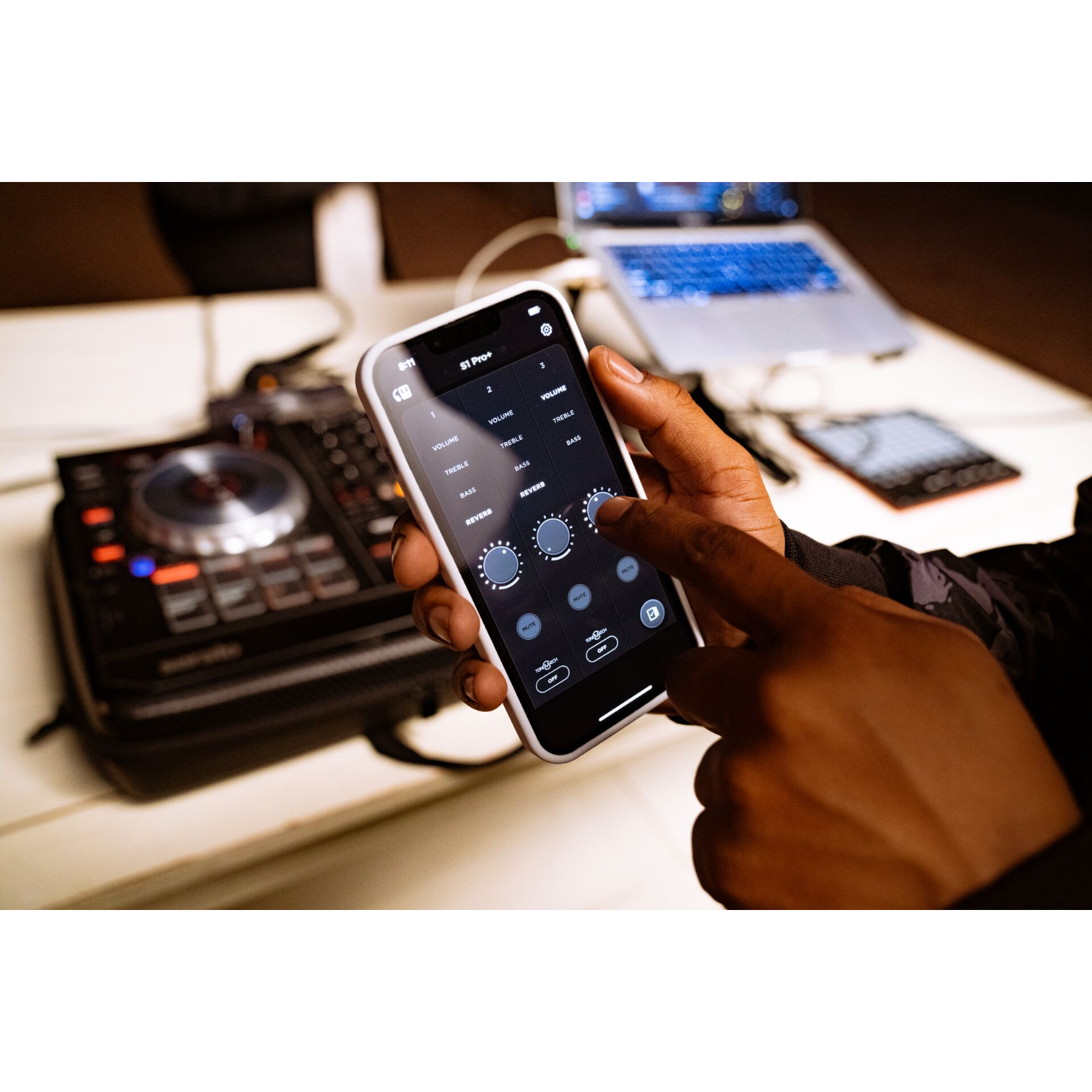 Hand van een persoon die een smartphone gebruikt naast DJ-apparatuur.