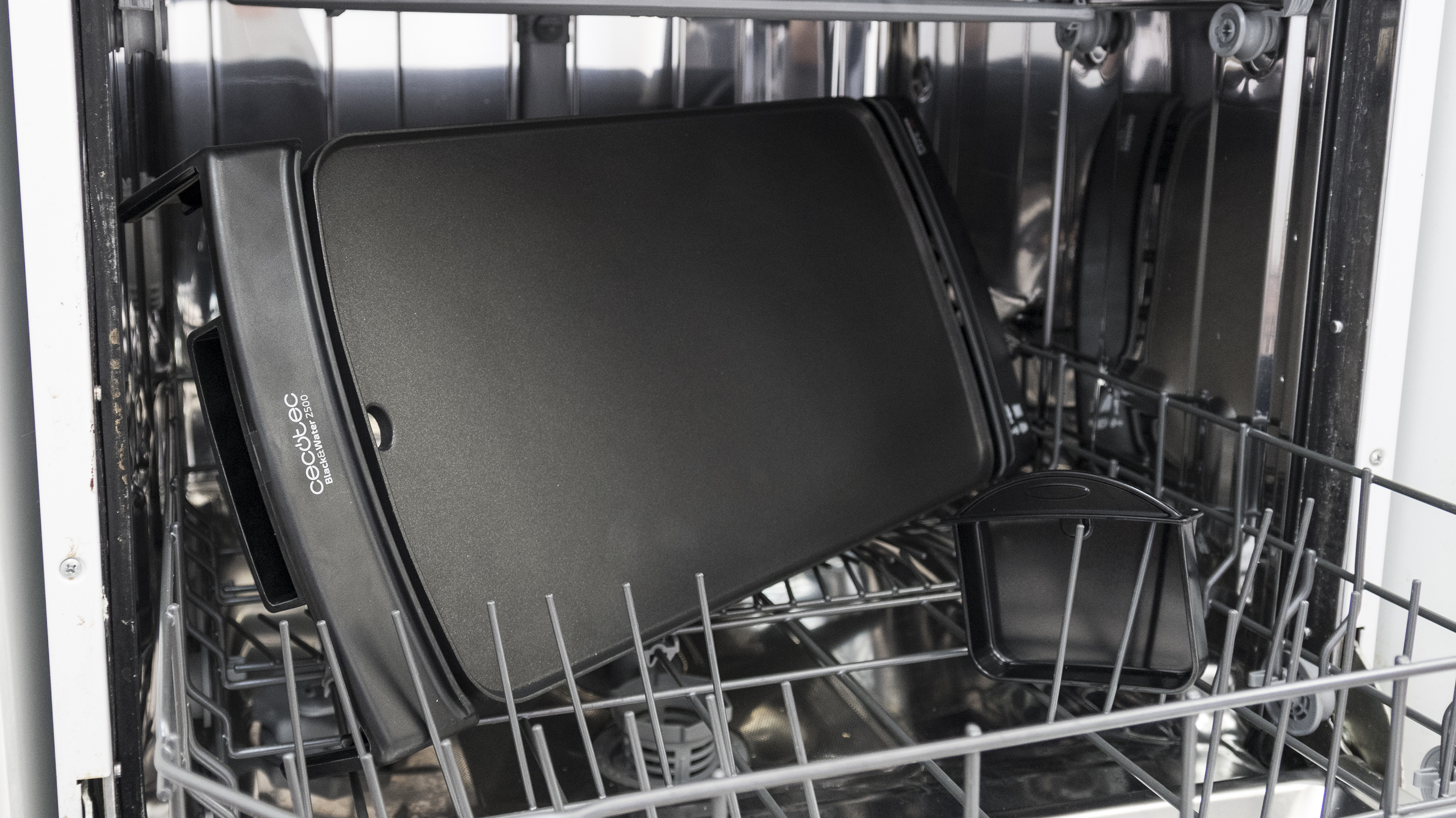 Plancha negra dentro de un lavavajillas. Otros platos están adentro. La plancha está en la rejilla inferior. Es una toma de primer plano.