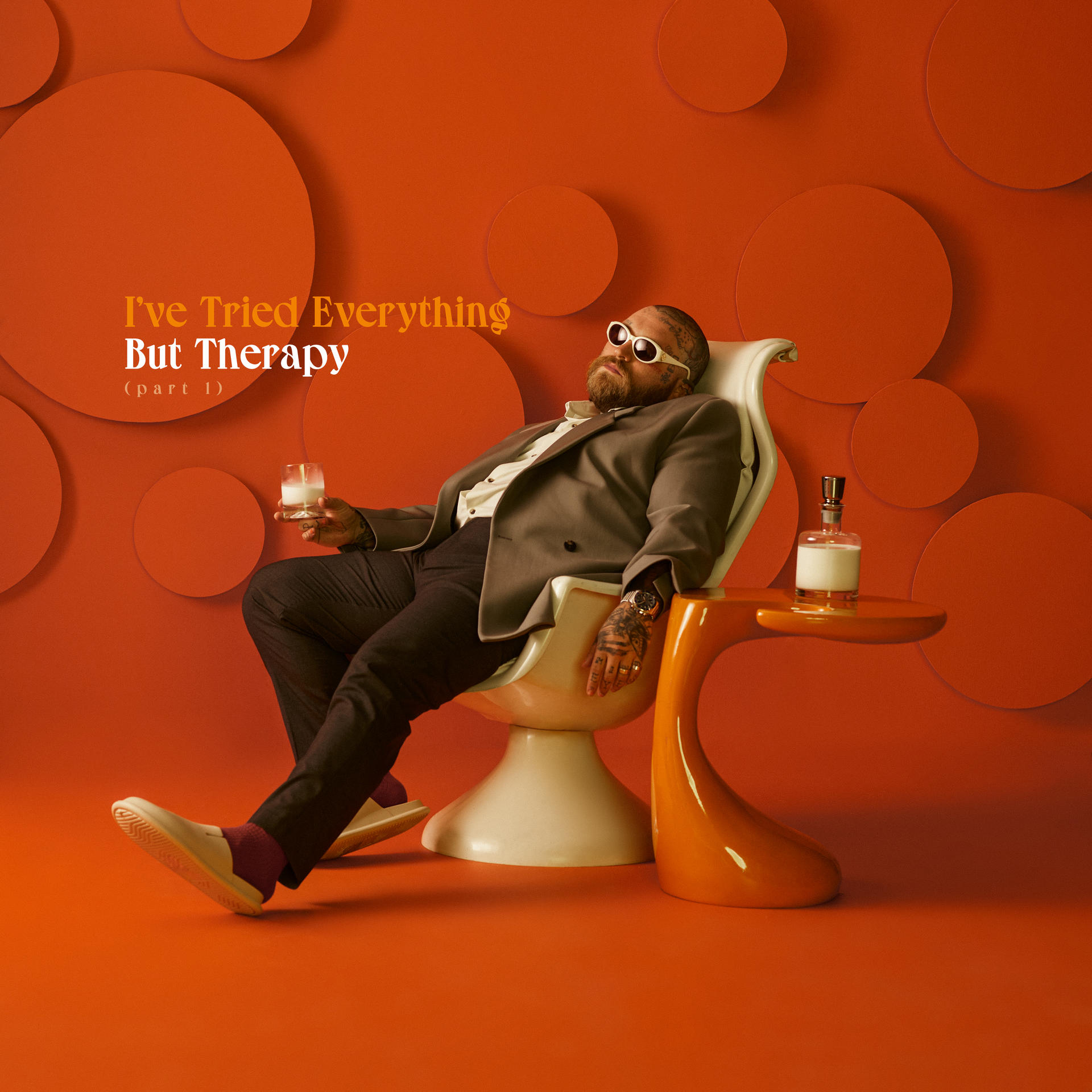 Mann in einem Stuhl mit Glas, auf rotem Hintergrund, mit dem Text 'I've Tried Everything But Therapy'.