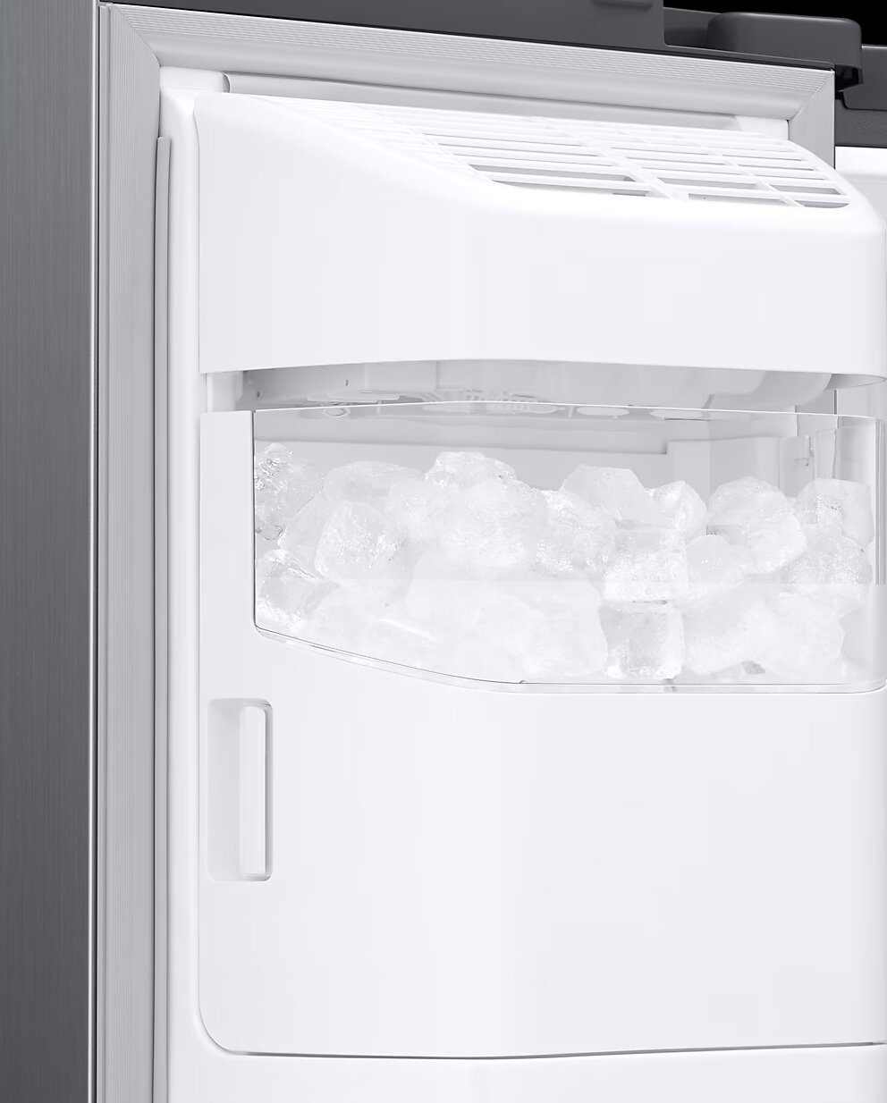 Zbliżenie białej kostkarki do lodu w lodówce wypełnionej kostkami lodu.