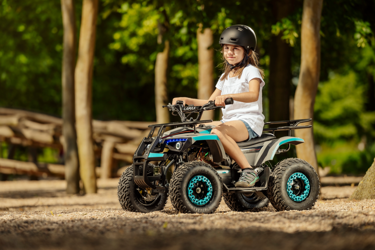 Egy lány sisakban kis ATV-t vezet egy úton. A háttérben fák sorakoznak. Az ATV türkizkék és szürke.