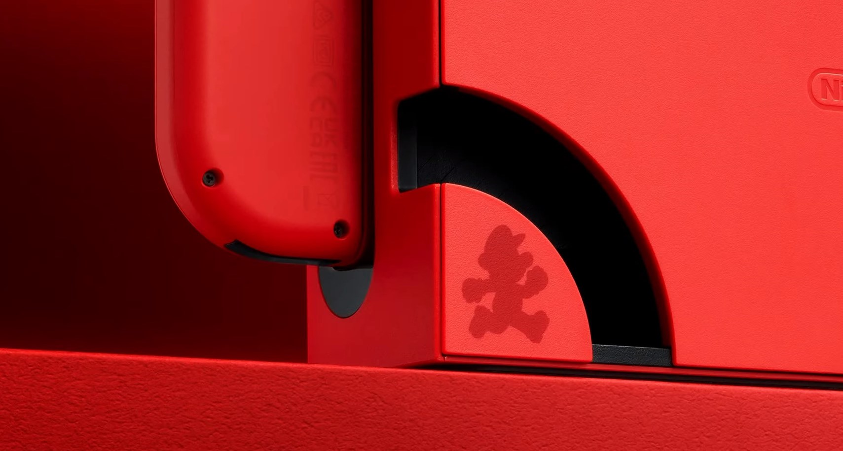 Una base roja de Nintendo Switch, con un Joy-Con rojo adjunto. Una silueta de Mario está en la parte delantera de la base.