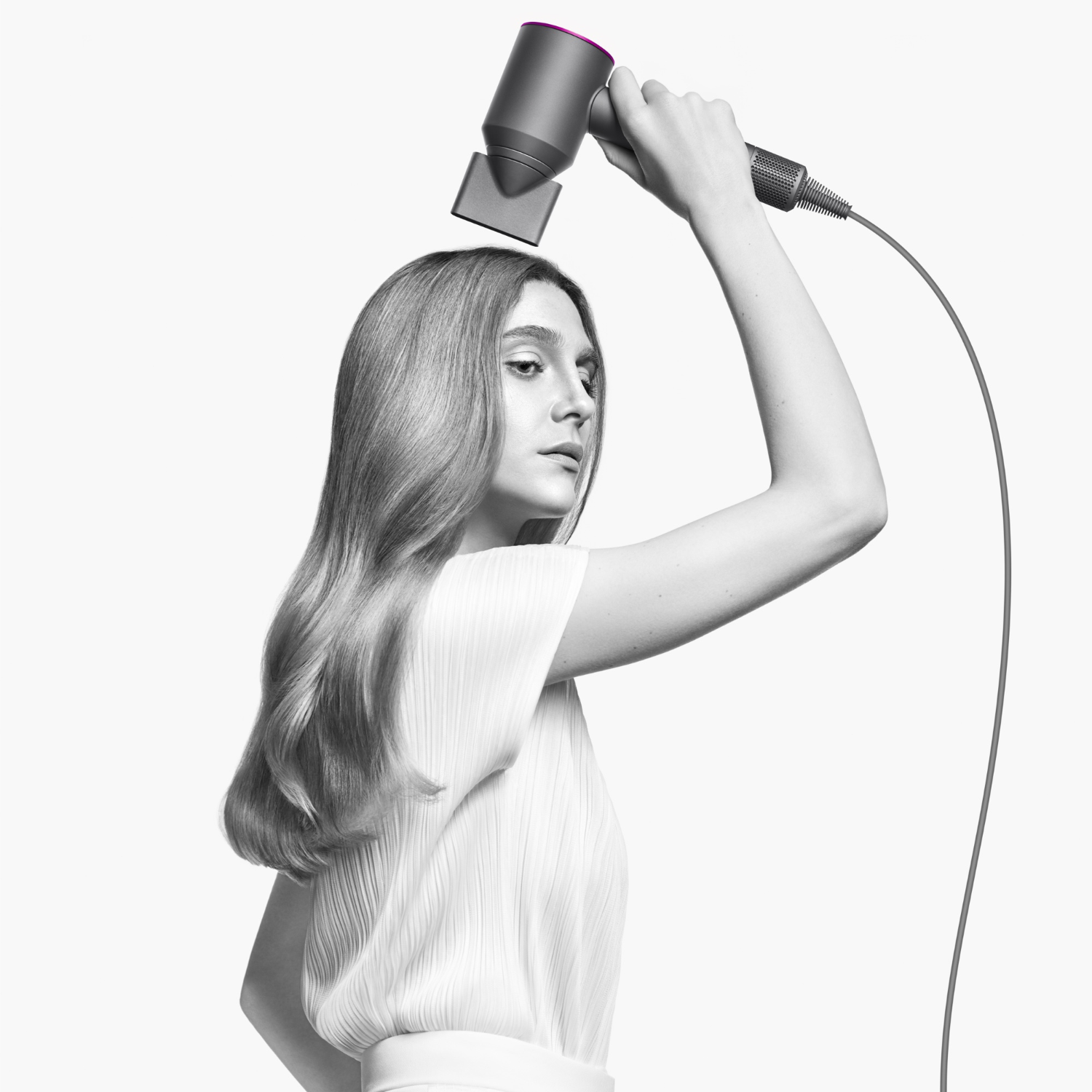 Woman using a black and gray hairdryer. The background is white.