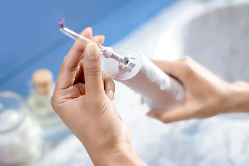 Zbliżenie osoby trzymającej biały irygator do jamy ustnej.