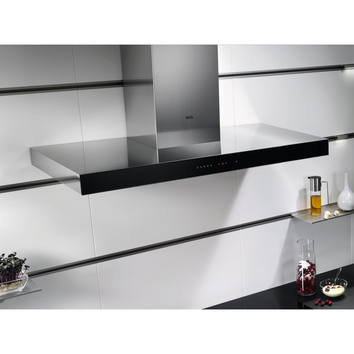 Küchenabzugshaube, Edelstahl, schwarze Verkleidung, an weiß gefliester Wand montiert. Beleuchtung sichtbar.