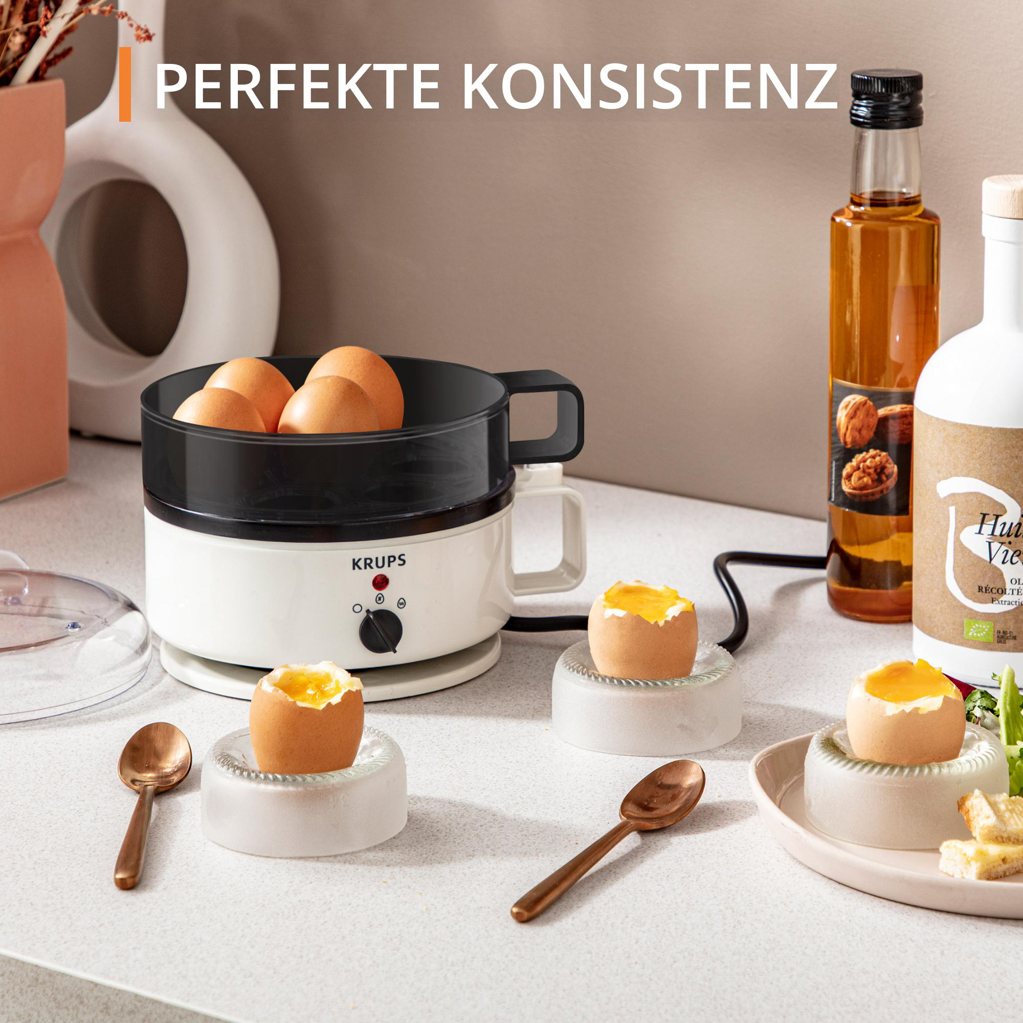Eierkocher mit Eiern, Löffeln, Ölflasche und Eiern auf dem Ständer.