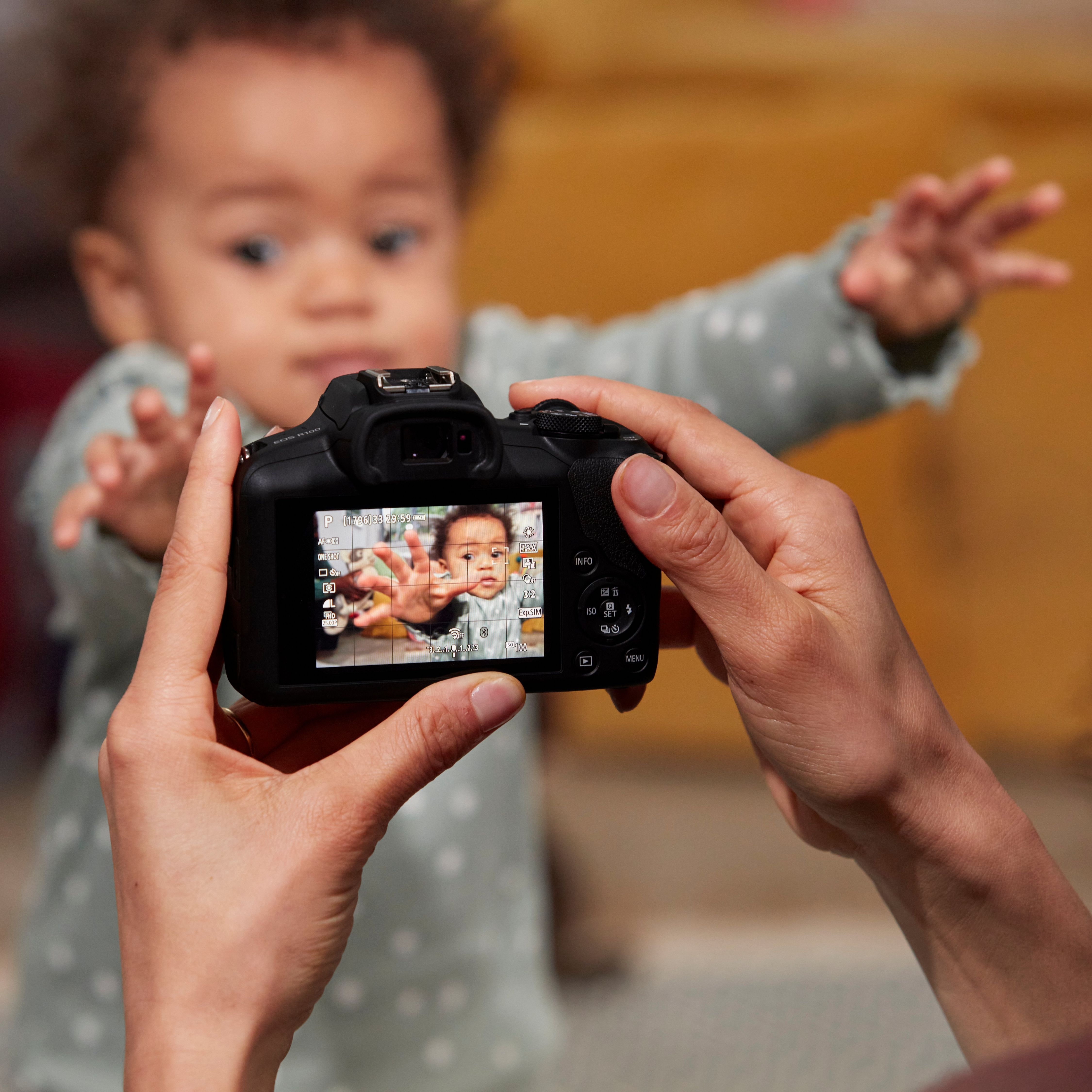 Une femme tient un appareil photo, prenant une photo d'un bébé tendant la main vers l'objectif. L'image du bébé est sur l'écran.