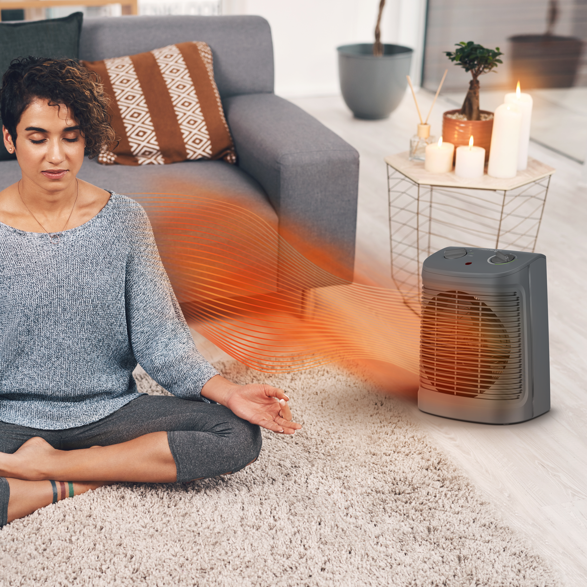 Mujer meditando en una habitación con calefactor, velas y sofá.