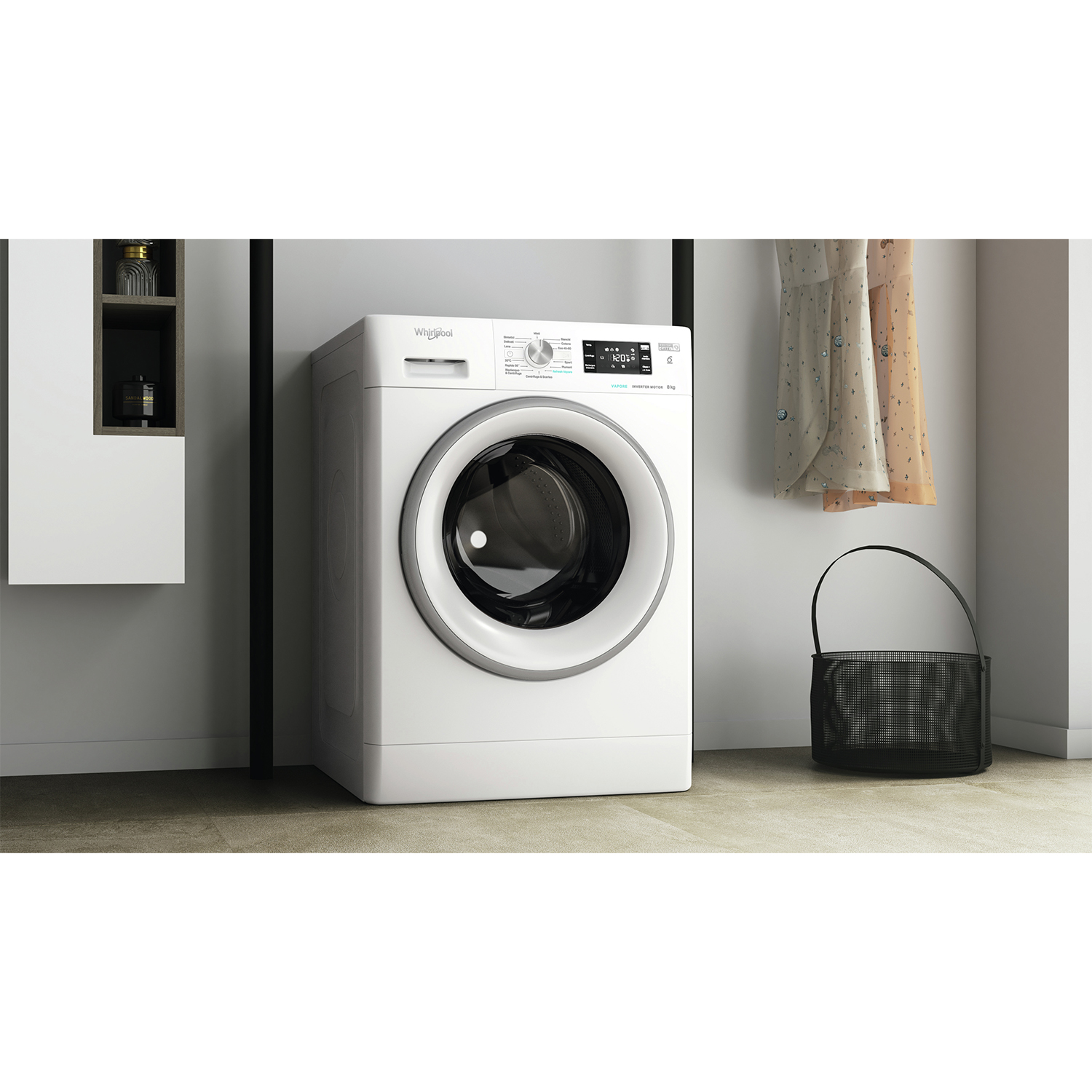 Una lavatrice Whirlpool bianca si trova in una stanza. Gli abiti sono appesi a destra, un cesto nero è davanti.