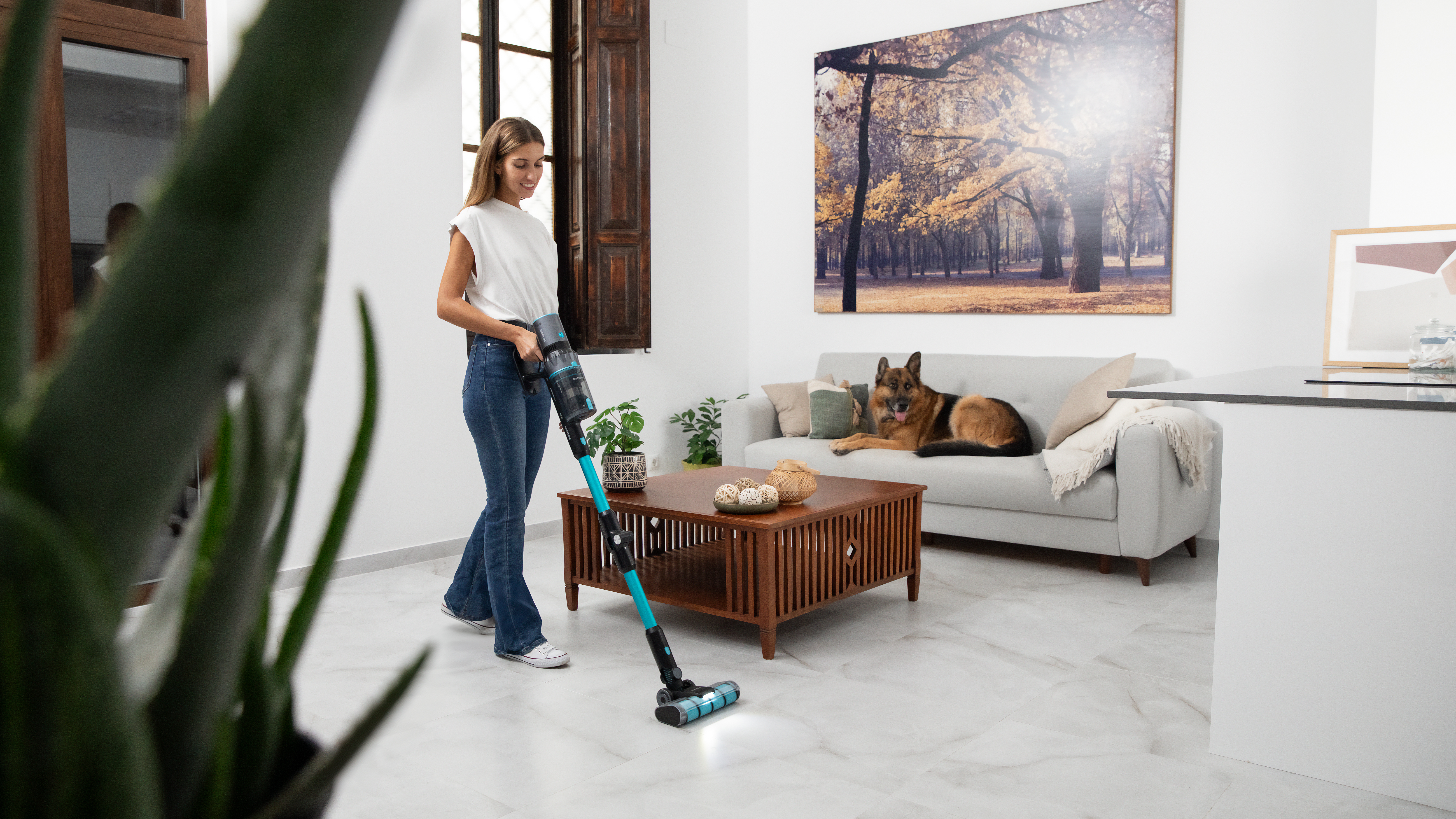 Mujer aspirando una habitación con un perro en el sofá.