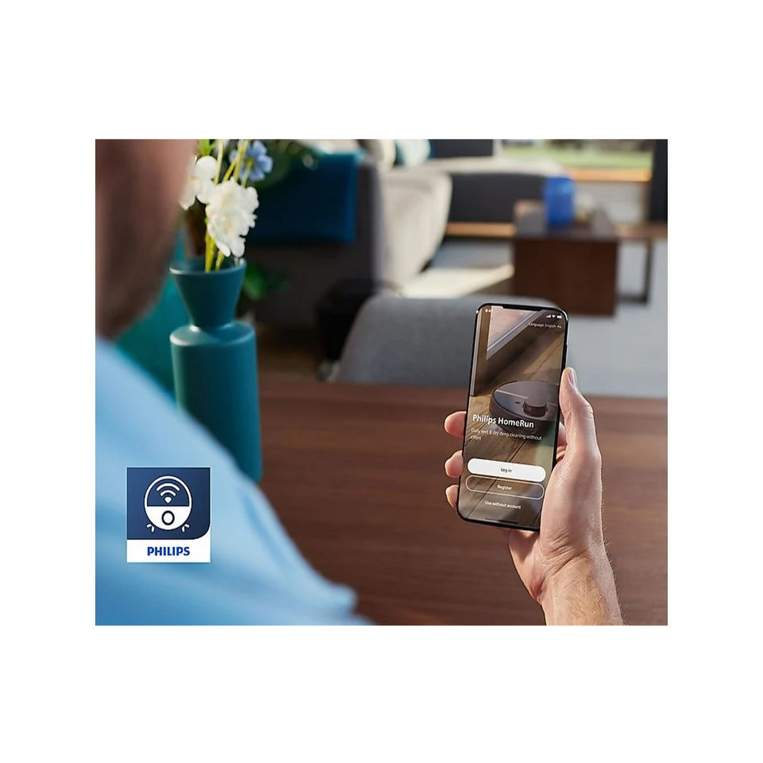 A person holds a phone displaying the Philips HomeRun app. Flowers and a blue vase are in the background.