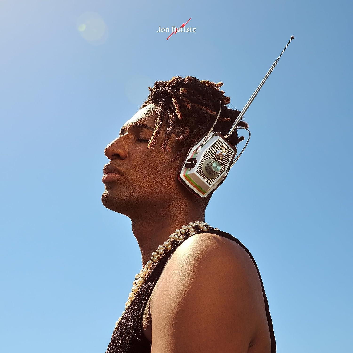 Férfi rádióhoz hasonló fejhallgatóval, gyöngy nyaklánccal, kék égbolttal. Cím: Jon Batiste.
