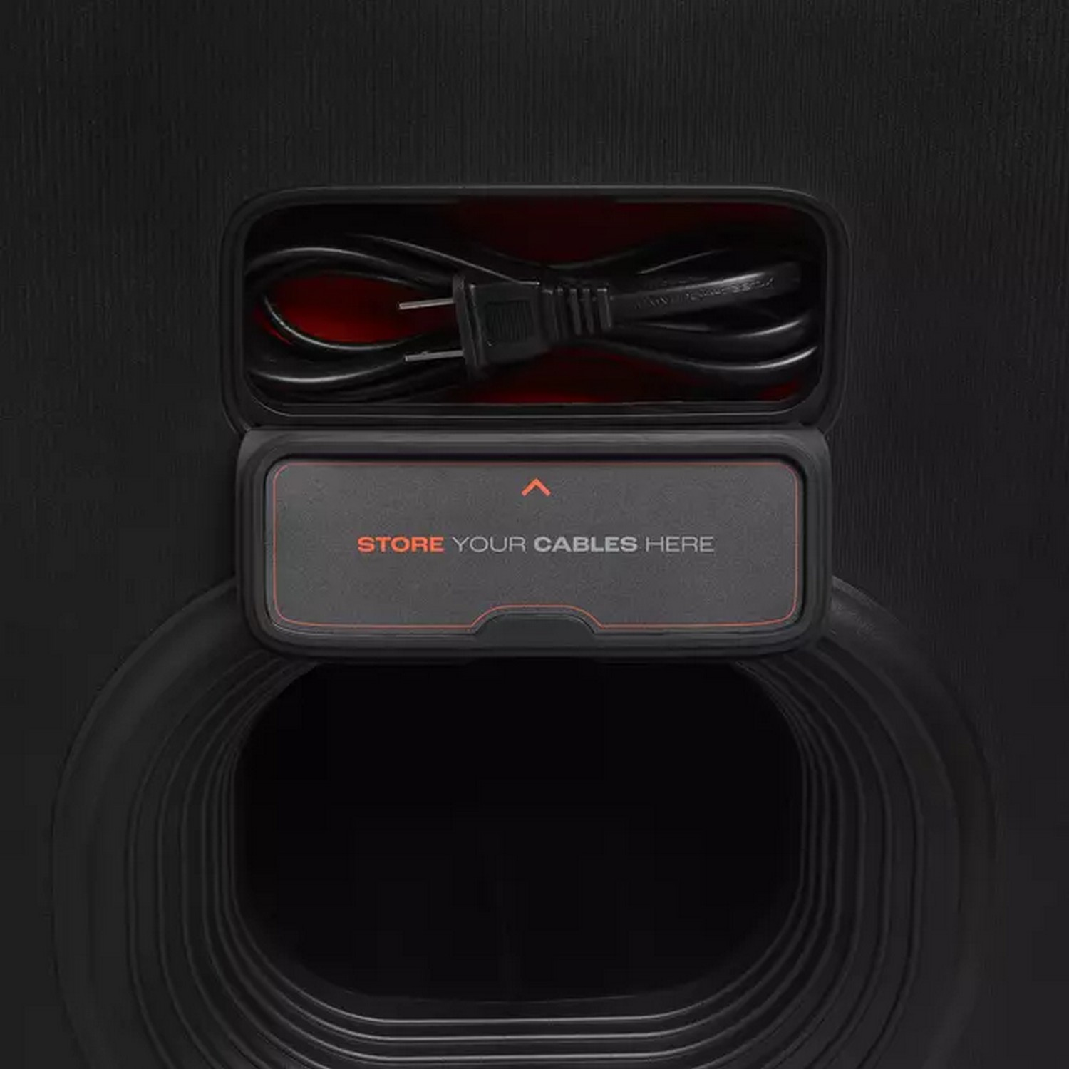 Open compartment on black speaker. Inside, a cable and a label that says, "STORE YOUR CABLES HERE".