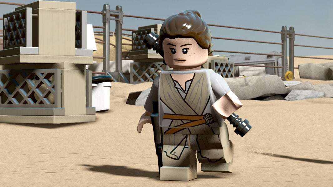 Figurka Lego Rey trzymająca miecze świetlne. Tło pustynne, beżowe. Budynek Lego z tyłu.