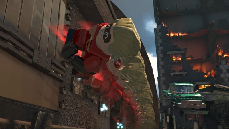 Postać Lego w czerwonym stroju wspina się po budynku. Płomienie i zielony samochód w tle.