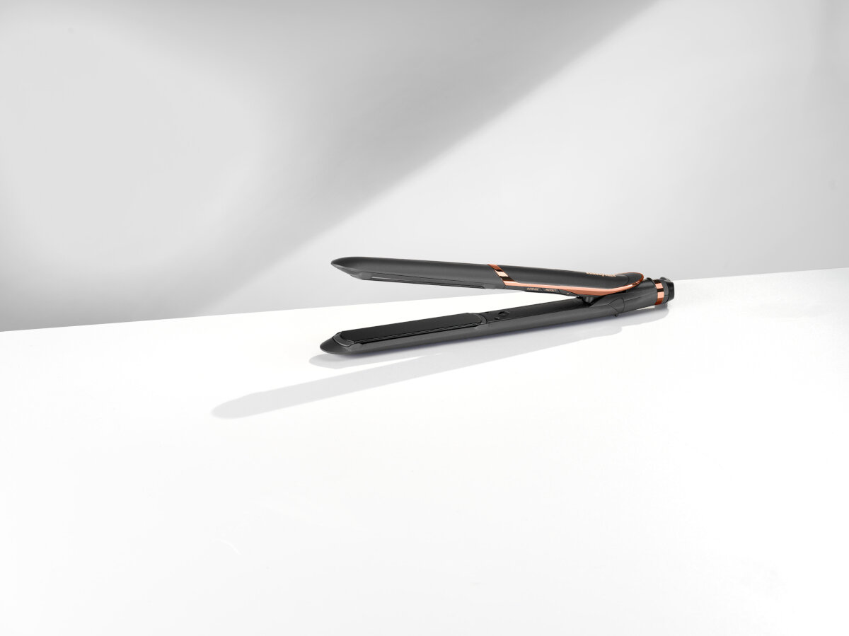 Czarna i różowo-złota prostownica do włosów na białej powierzchni. Białe tło.