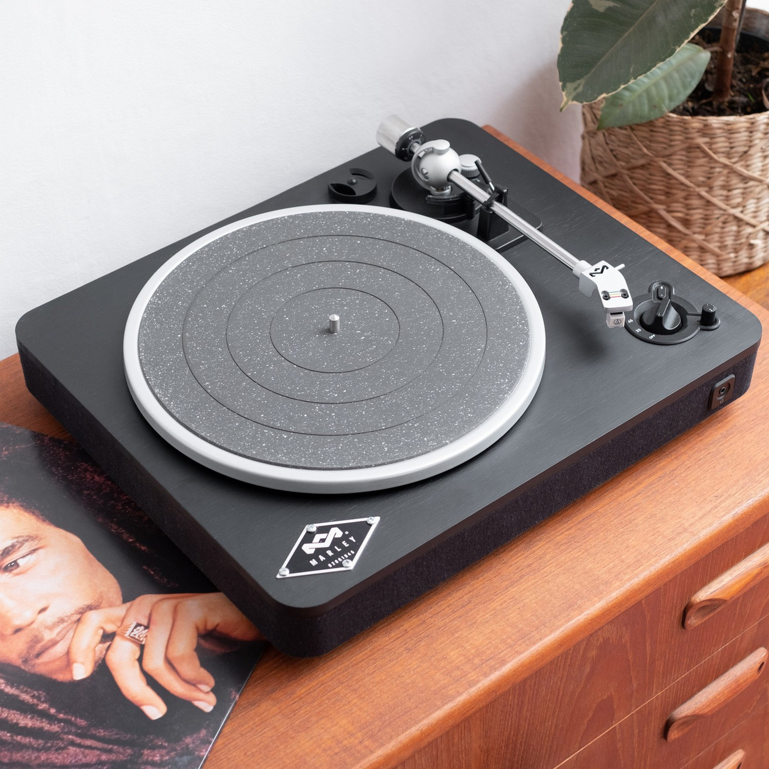 Black turntable on a wooden surface, with a record and plant.