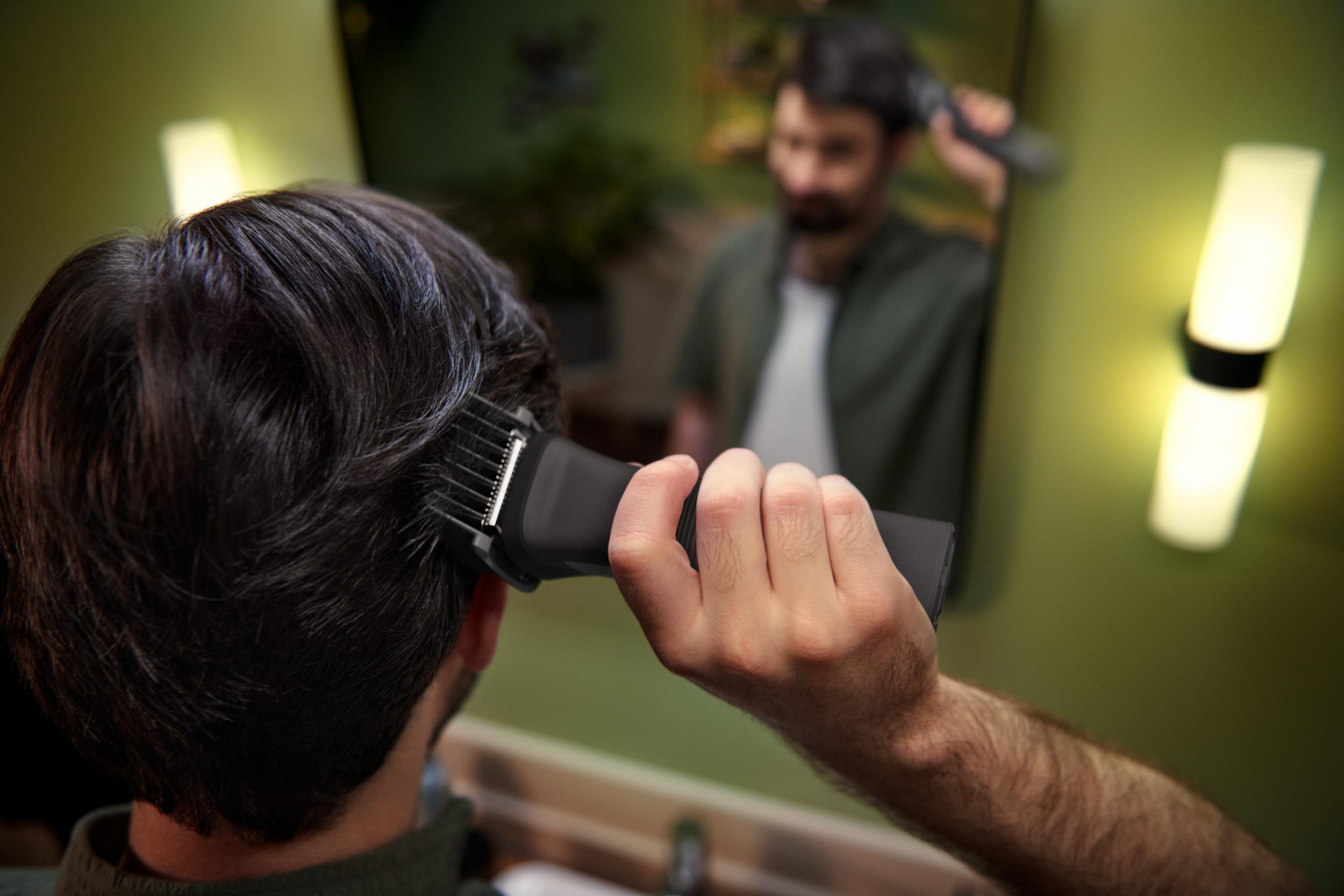 Mann, der im Spiegel einen schwarzen Haarschneider benutzt.