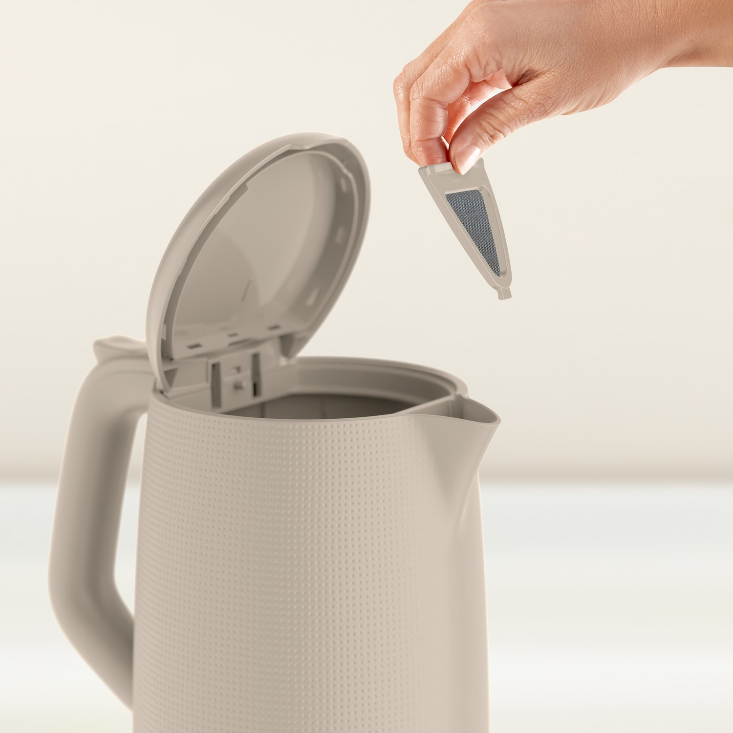 A person's hand is placing a filter into a white electric kettle. 
