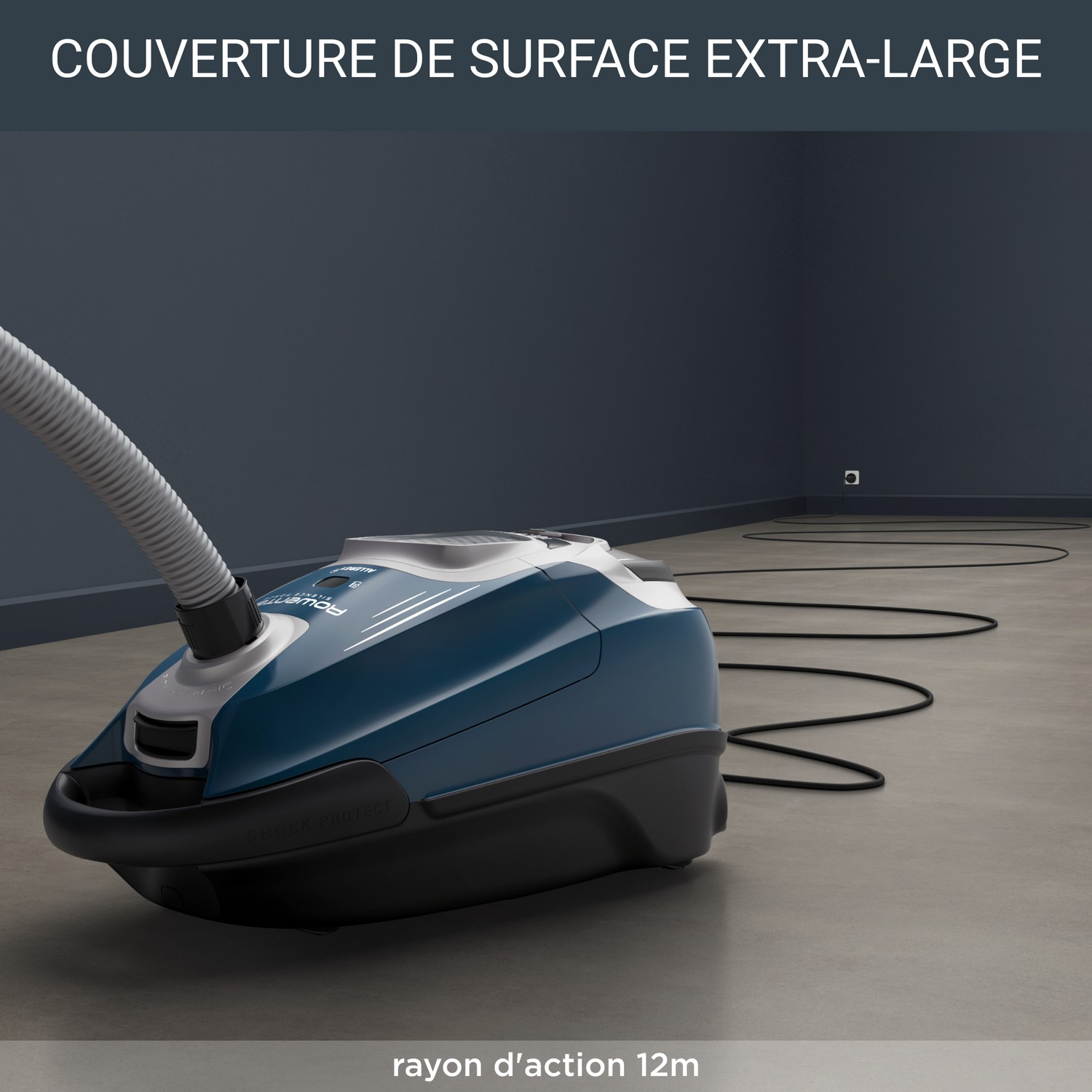 Aspirateur bleu dans une pièce avec sol gris et mur bleu foncé. Texte : 'Couverture de surface extra-large'.