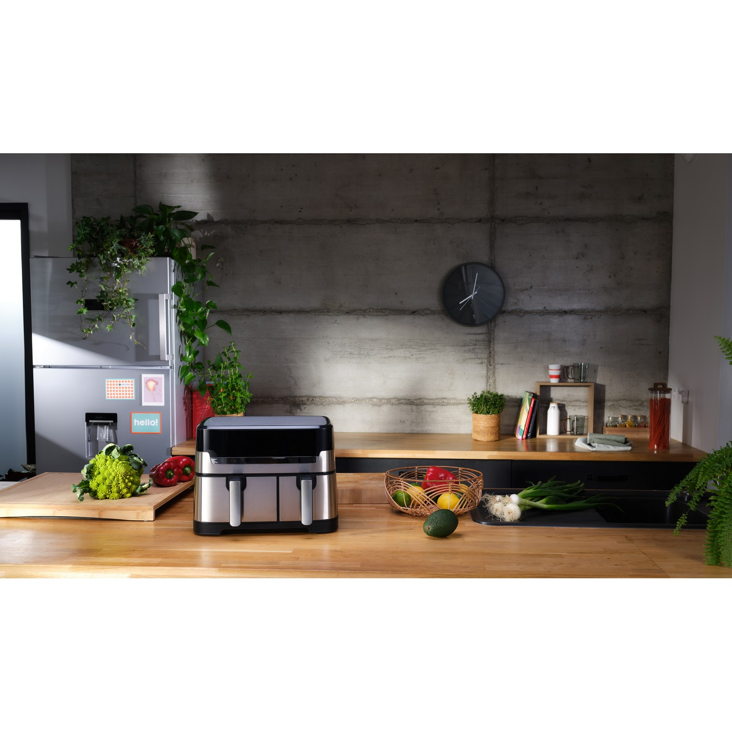 Scène de cuisine avec une friteuse à air, des plantes et divers fruits et légumes sur un comptoir en bois.
