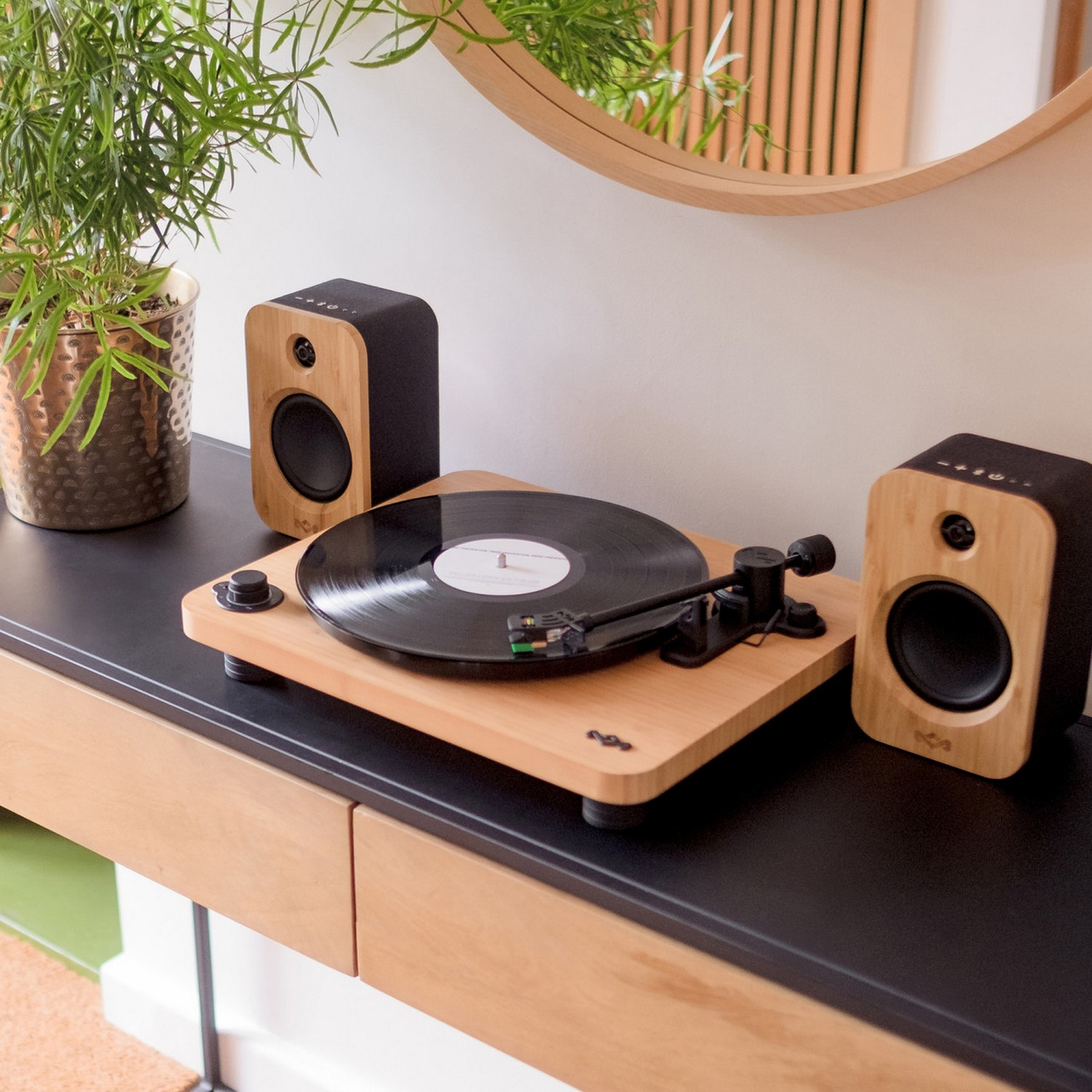 Een platenspeler met een plaat die afspeelt, twee luidsprekers en een plant op een houten oppervlak.