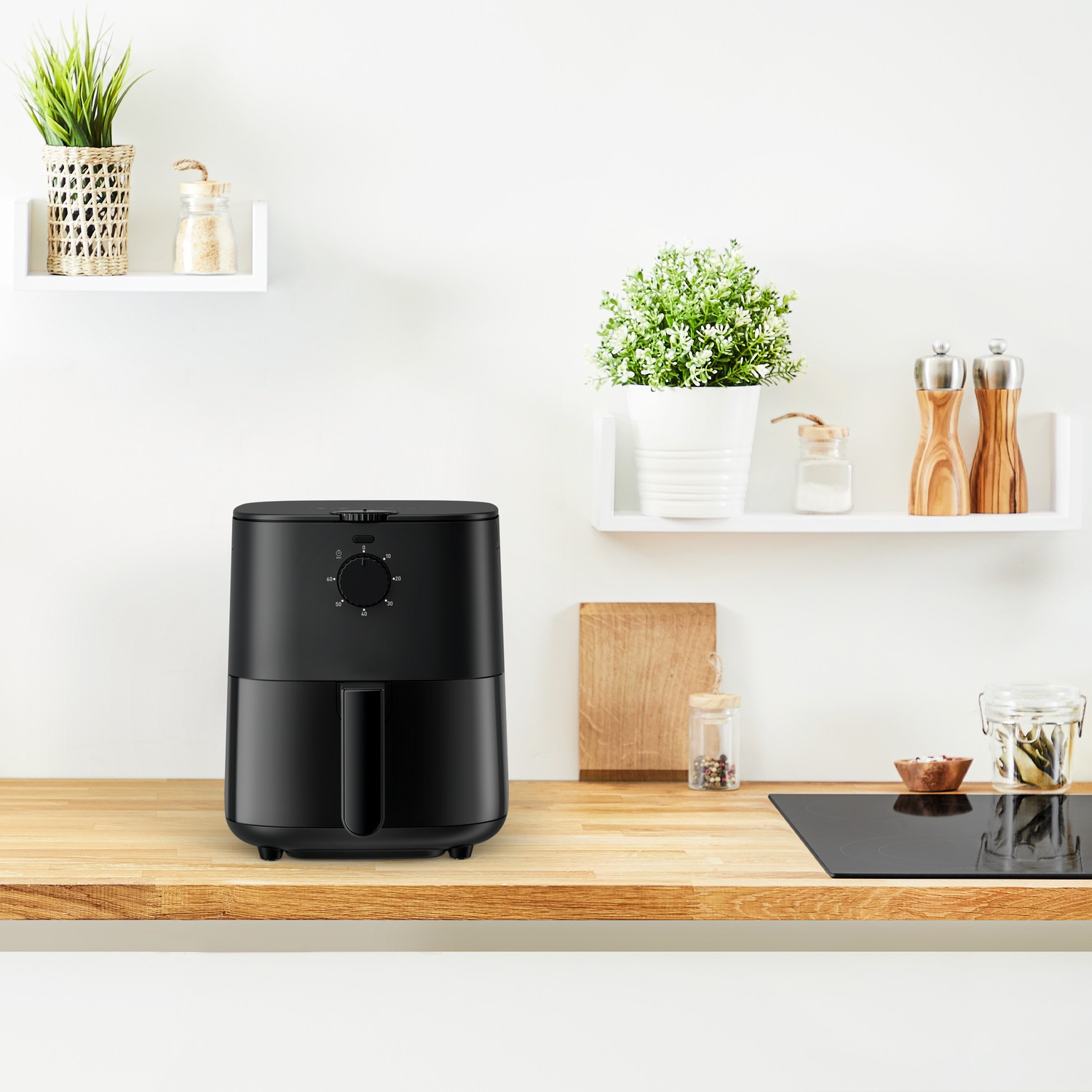 Een zwarte airfryer op een houten aanrecht, met planten en planken op de achtergrond.