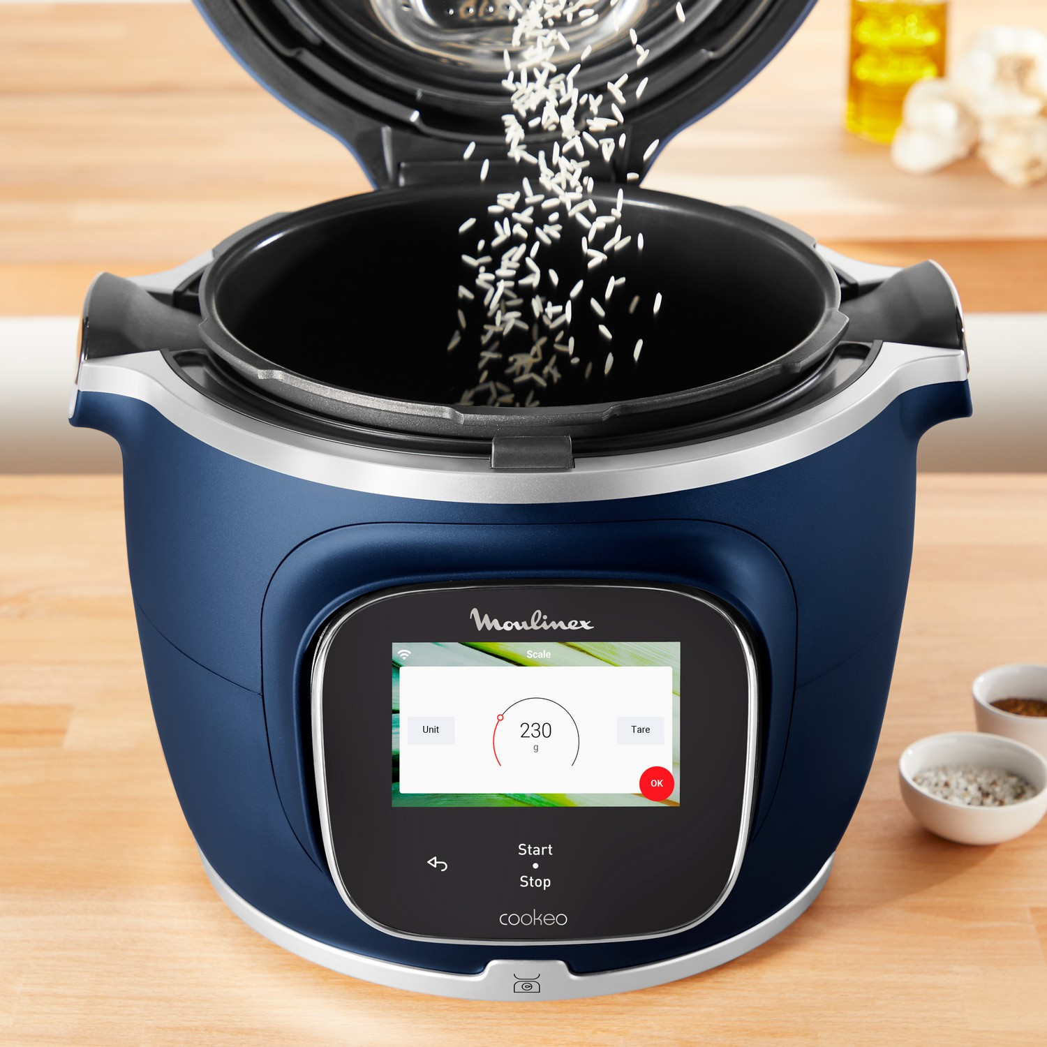 A blue Moulinex Cookeo smart multicooker with rice pouring into it, displaying a screen.