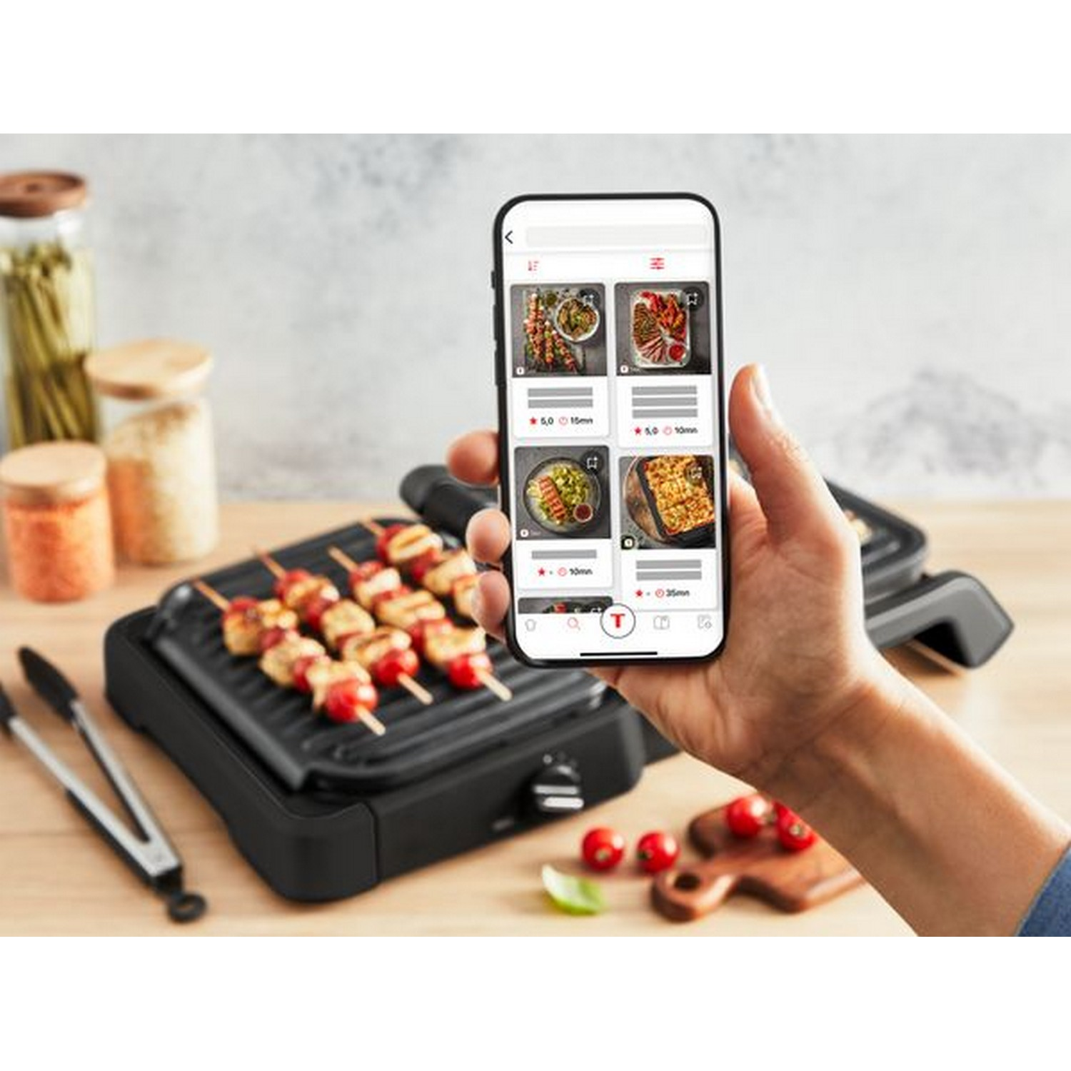 A person holding a phone showing food recipes next to a grill with skewers.