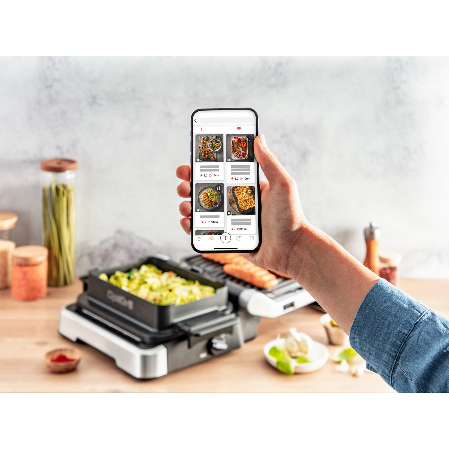 Hand die een telefoon vasthoudt met een kookrecept-app, eten op de grill en ingrediënten.