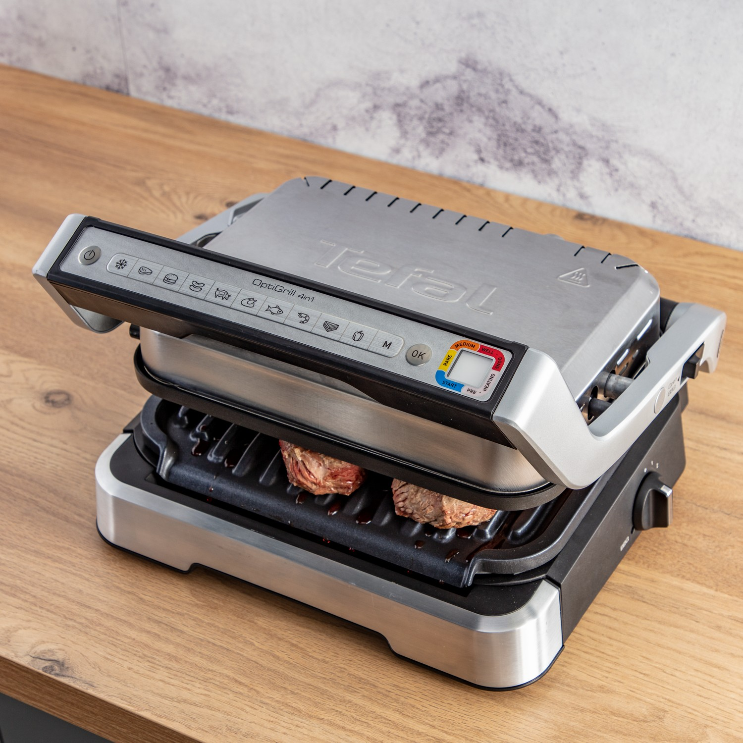 Tefal OptiGrill 4-in-1. Grill open, met twee steaks. Houten tafel.