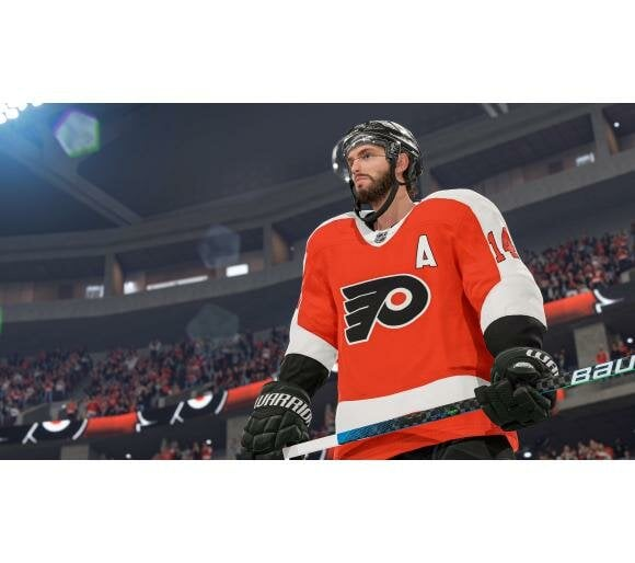 Hokeista w pomarańczowej koszulce na lodzie.  W tle tłum na stadionie.