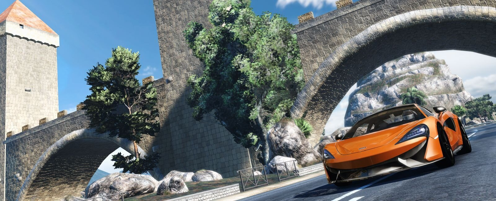 Pomarańczowy samochód sportowy jadący drogą z kamiennym mostem i wieżą w słoneczny dzień.