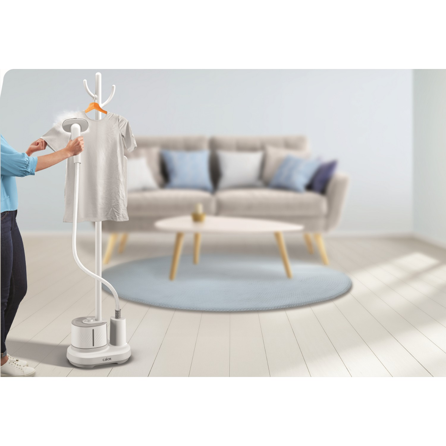 A person steaming a shirt with a Calor garment steamer in a room with furniture.