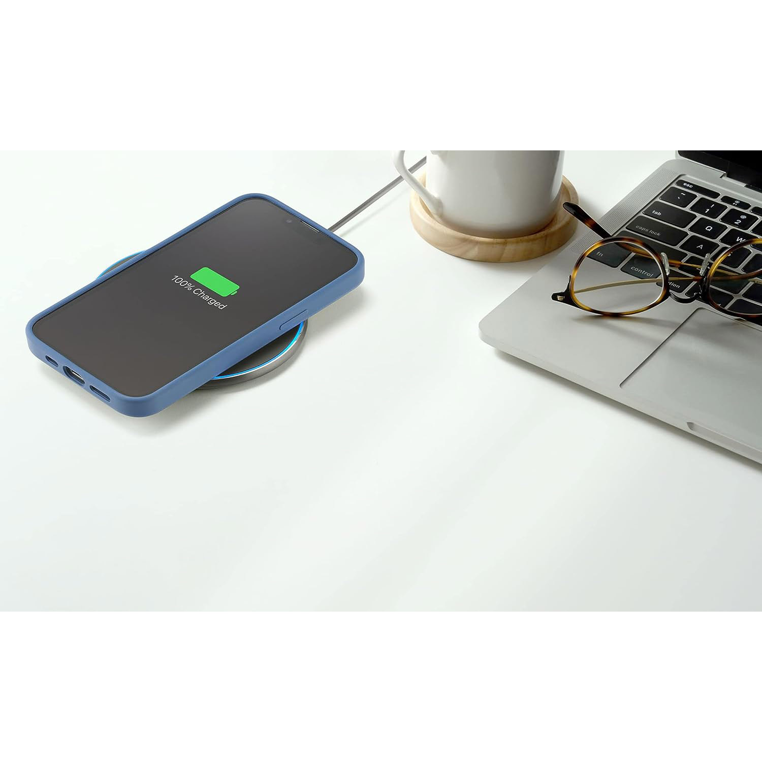 Uno smartphone in una custodia blu si carica su un caricatore wireless, con un laptop nelle vicinanze.