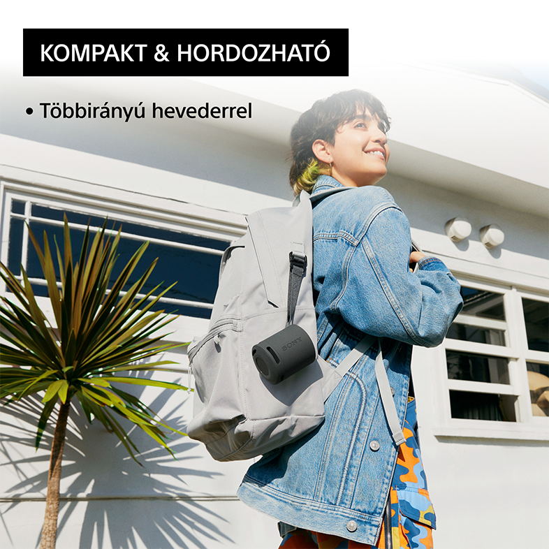 Nő szürke hátizsákkal és egy kis fekete hangszóróval, a szabadban áll pálmafával.