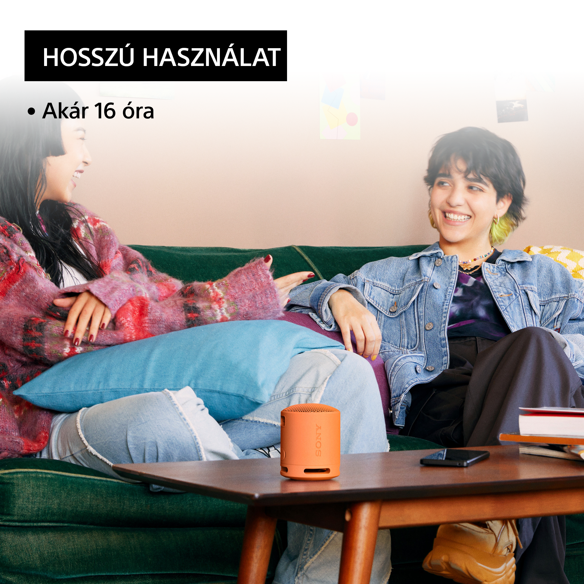 Két nő egy zöld kanapén. Egy narancssárga hangszóró az asztalon. Szöveg: Hosszú használat, akár 16 óra.