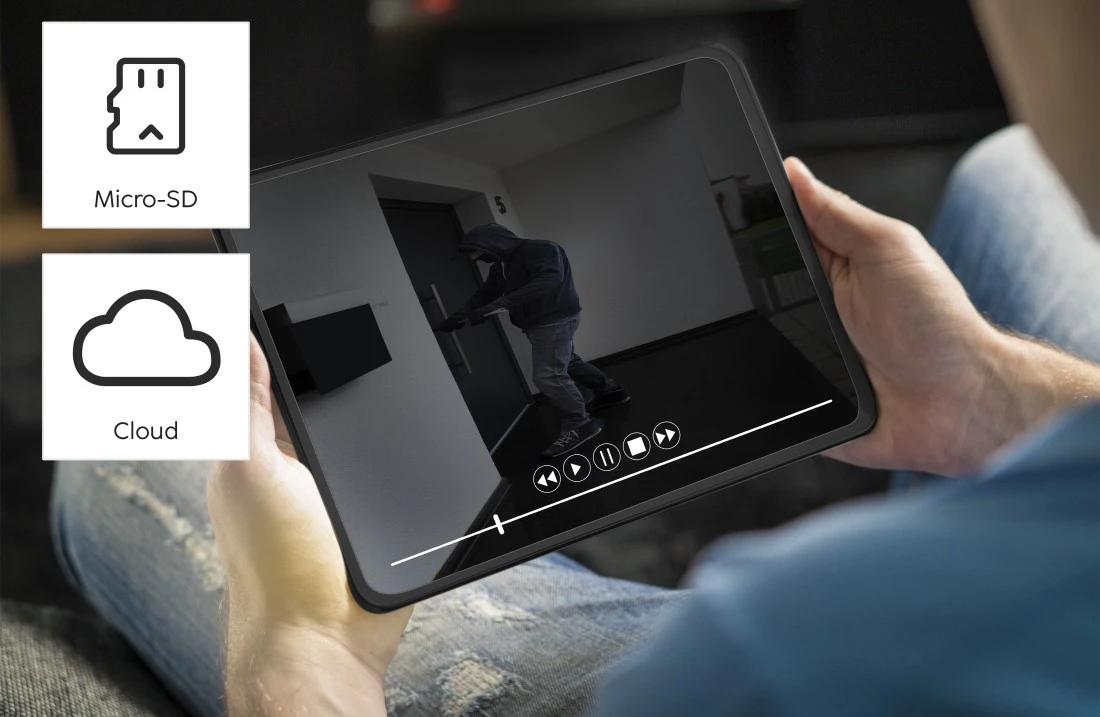Egy személy egy táblagépet tart, amely egy otthoni biztonsági kamera videófolyamát mutatja ikonokkal.