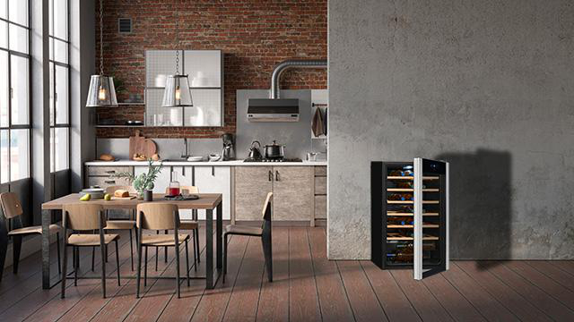 Moderne Küche mit Weinkühlschrank. Ziegelmauer, Holzboden. Tisch und Stühle sind sichtbar.