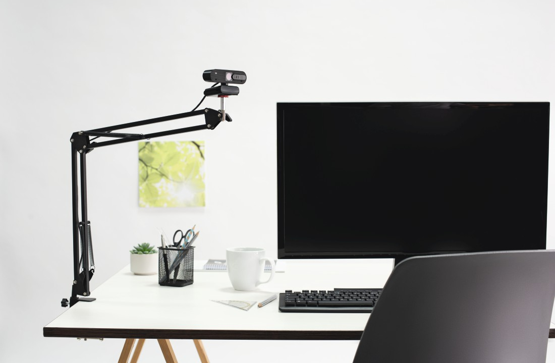 Egy íróasztal webkamerával és számítógép-monitorral, fehér háttérrel.