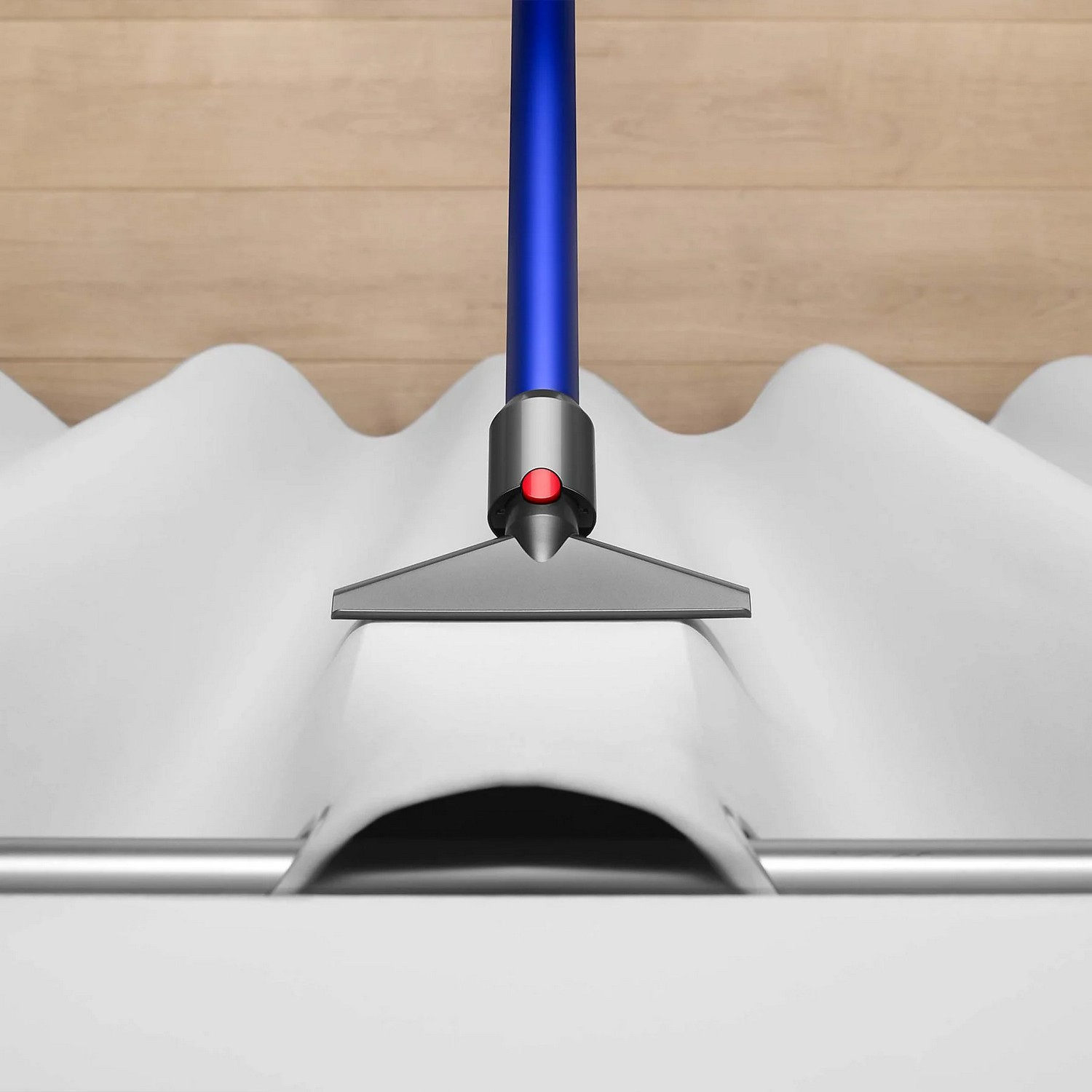Un aspirateur bleu nettoie une surface blanche et ondulée avec une barre argentée en bas.