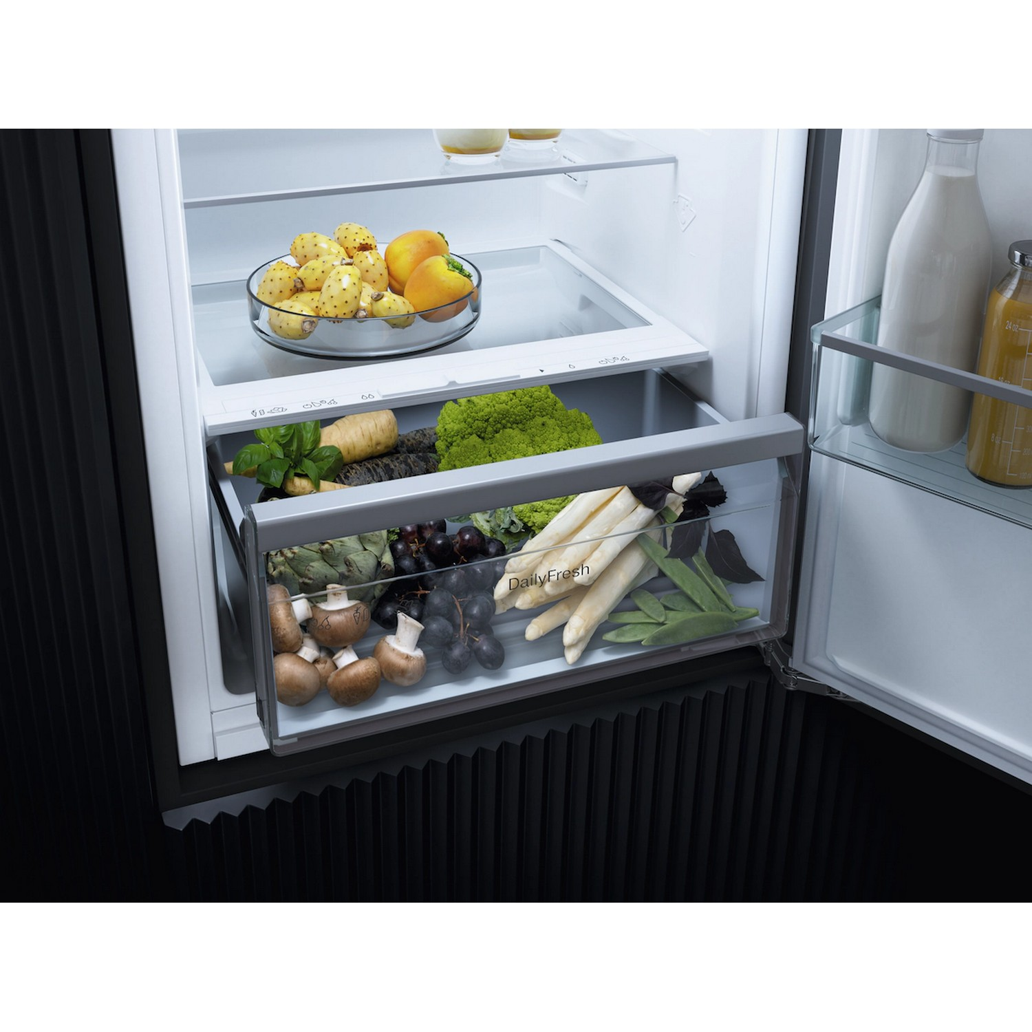 Tiroir de réfrigérateur rempli de légumes et de fruits. Au-dessus, un bol en verre avec des fruits est visible.