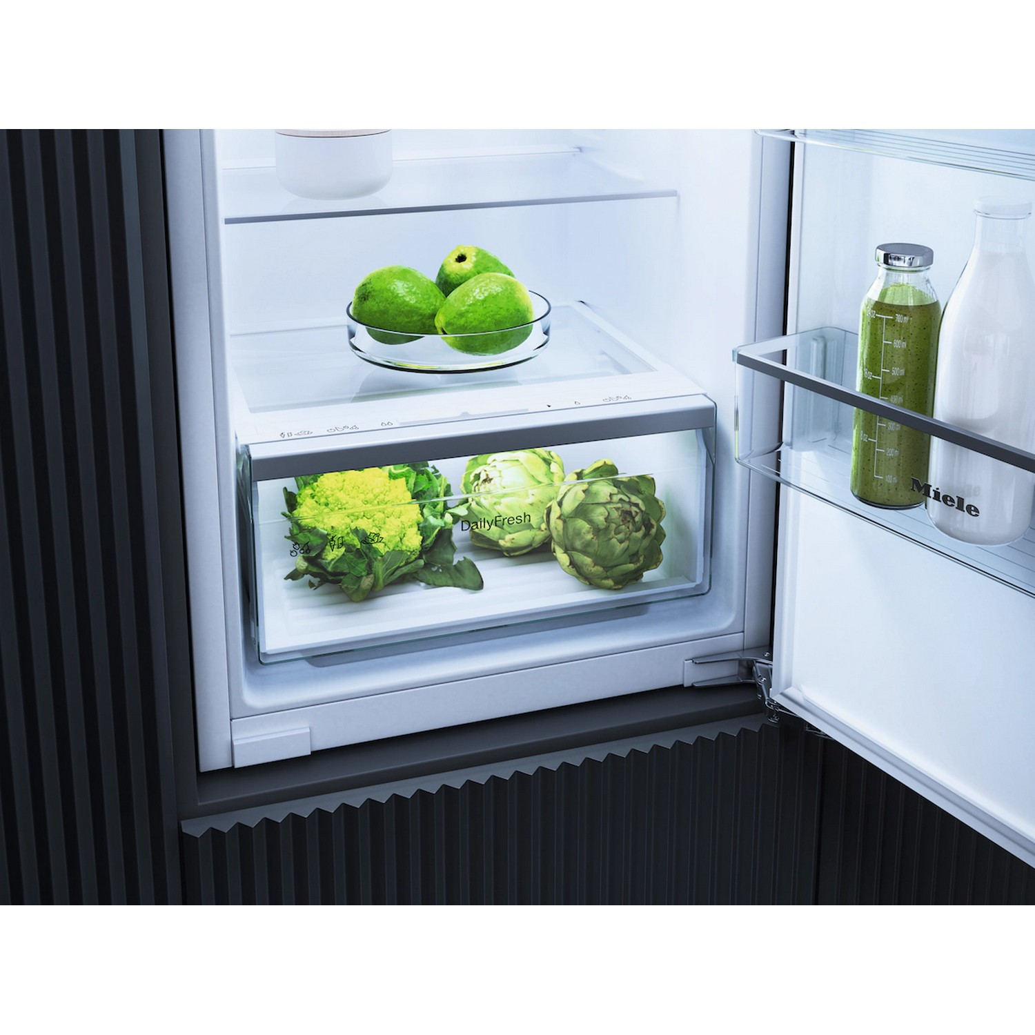 Intérieur de réfrigérateur avec un tiroir de légumes et un bol de fruits, avec deux bouteilles dans la porte.