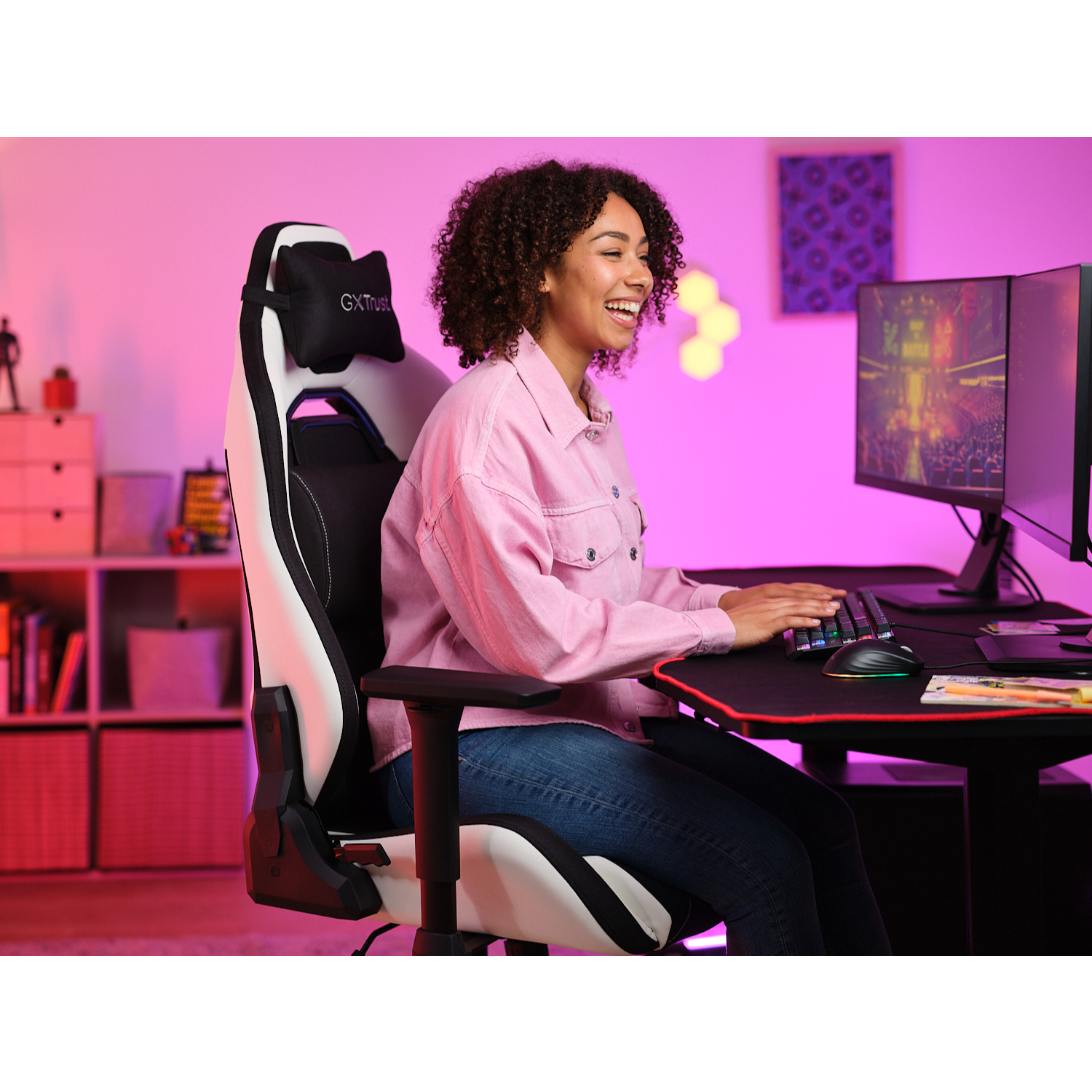 Woman smiling, gaming at a desk with a gaming chair and monitors.