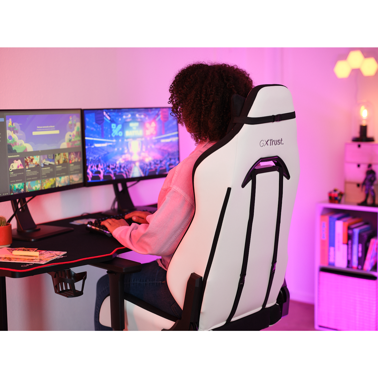 A person sitting in a white gaming chair, using a computer with two monitors. 