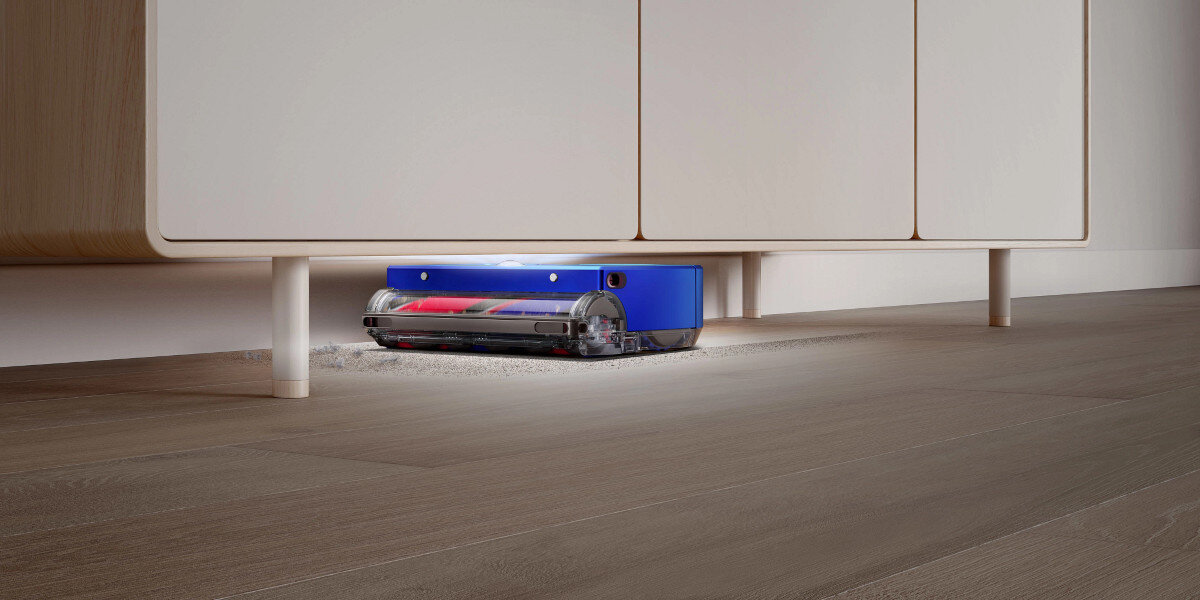 Robot odkurzający pod białą szafką na drewnianej podłodze.