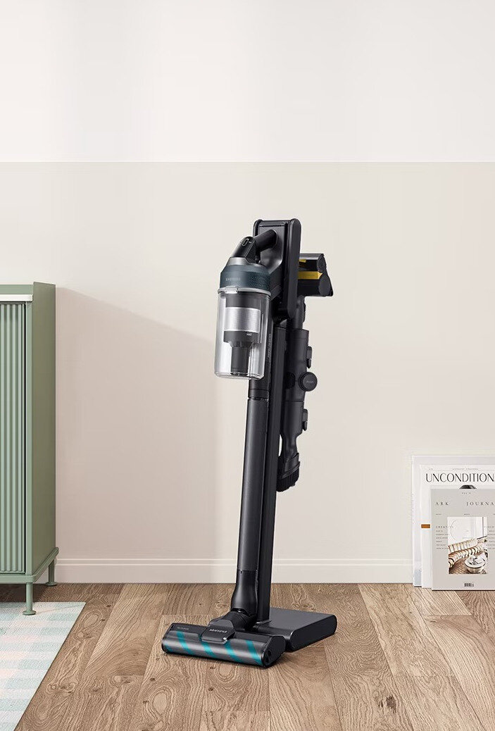 Bezprzewodowy odkurzacz Samsung stoi w pozycji pionowej na drewnianej podłodze. Widoczna jest zielona szafka.