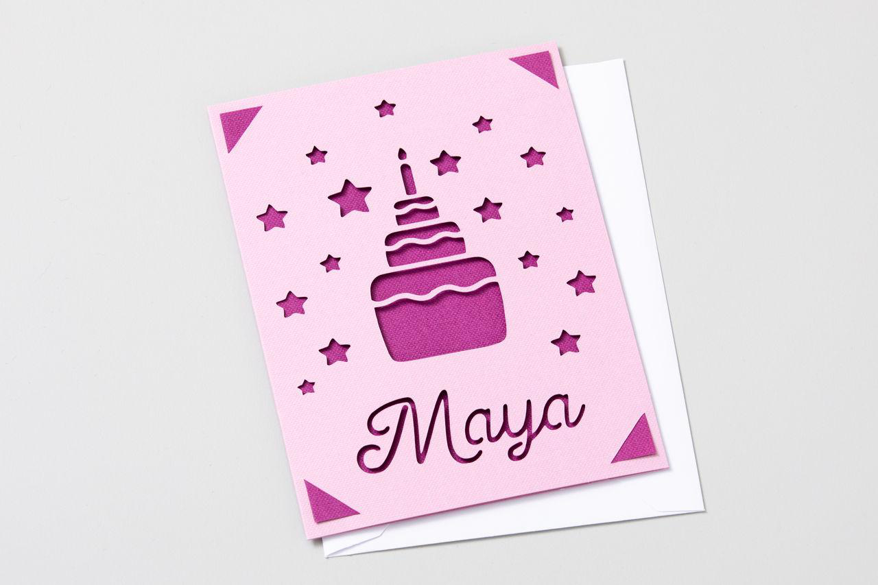 Geburtstagskarte mit ausgeschnittenem Kuchen, Sternen, Maya-Text, rosa Papier, weißem Umschlag, weißem Hintergrund.