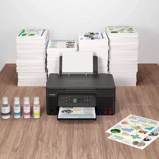 Drukarka Canon ze stosami papieru, wkładami atramentowymi i wydrukowanymi dokumentami na drewnianym stole.