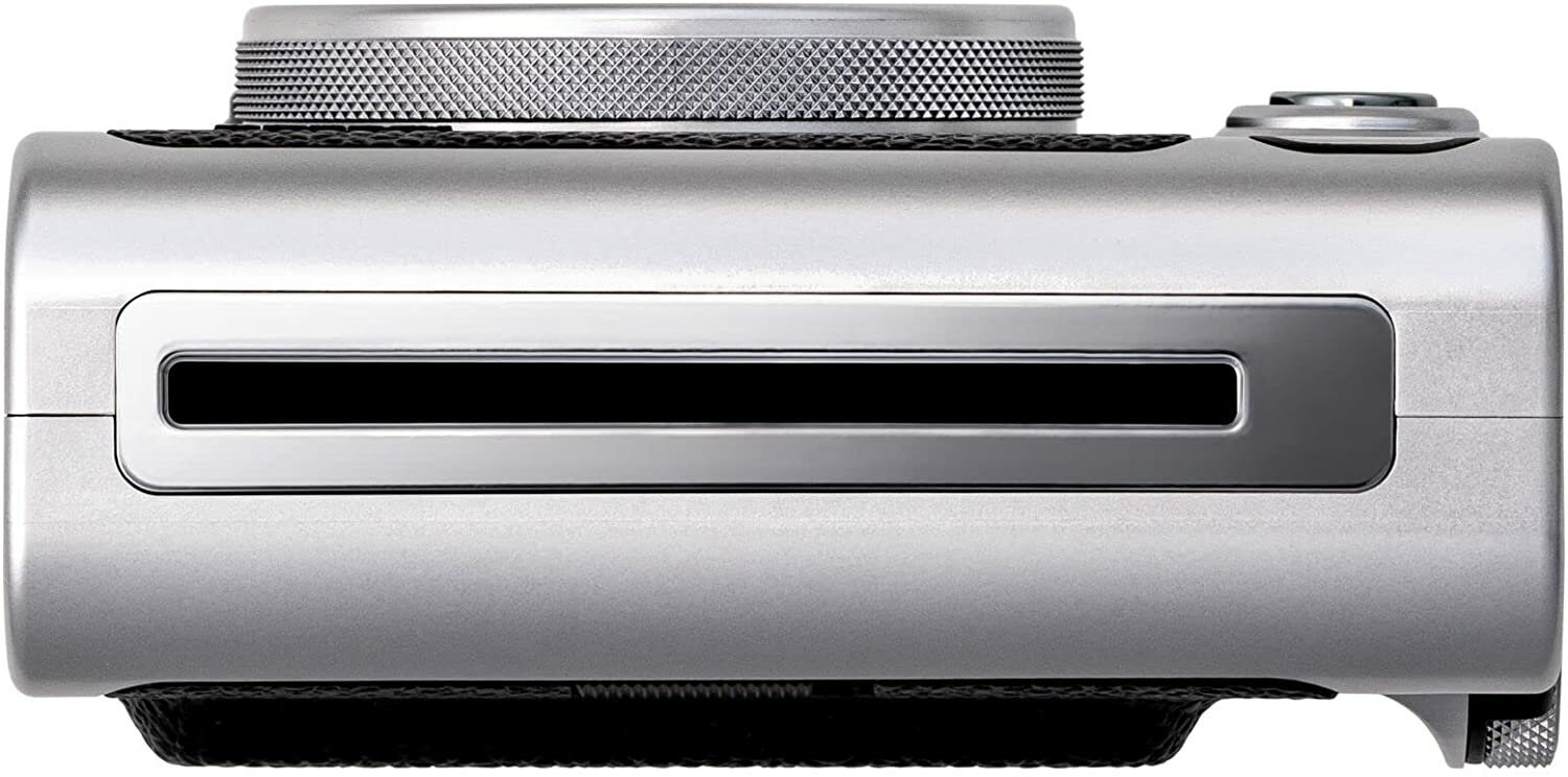 Srebrny aparat, widok z góry, z czarnym uchwytem i obiektywem na czarnym tle.